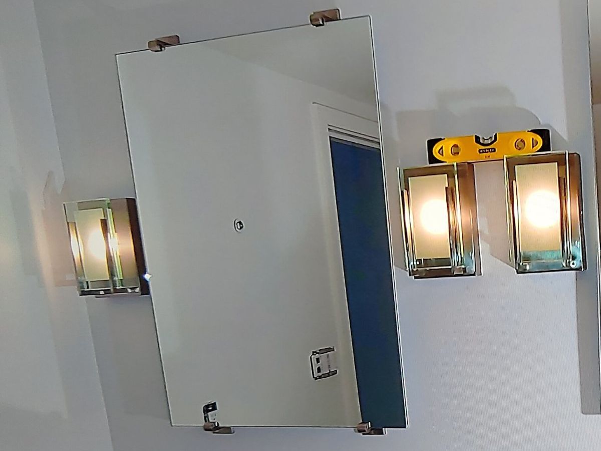 Frameless bathroom mirror and wall sconces mounted level over a vanity