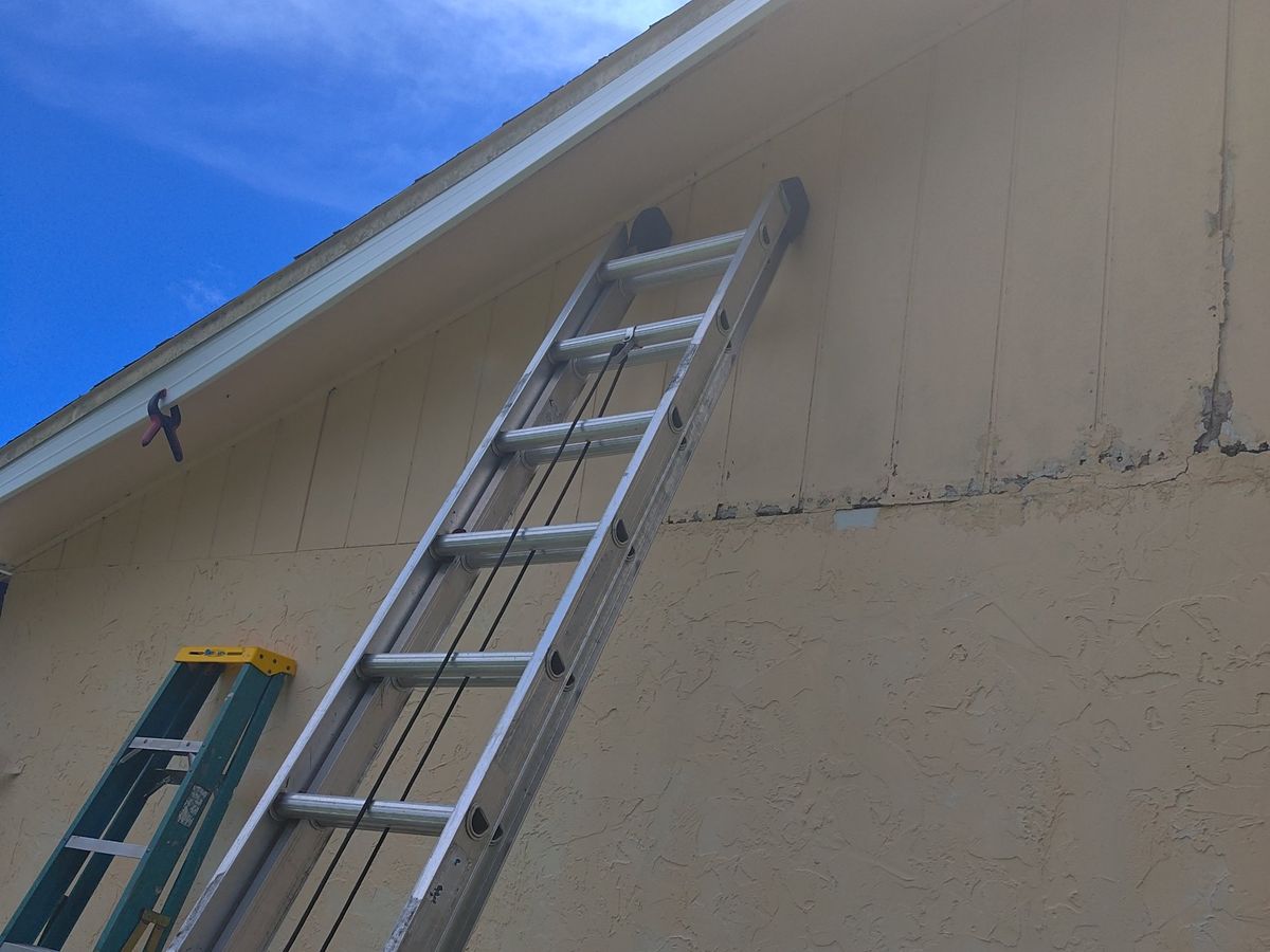 Ladders against a house gable where fascia and siding are being repaired