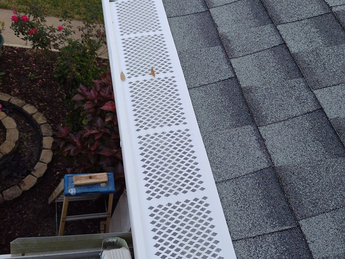 Perforated gutter guards installed along a shingle roof edge